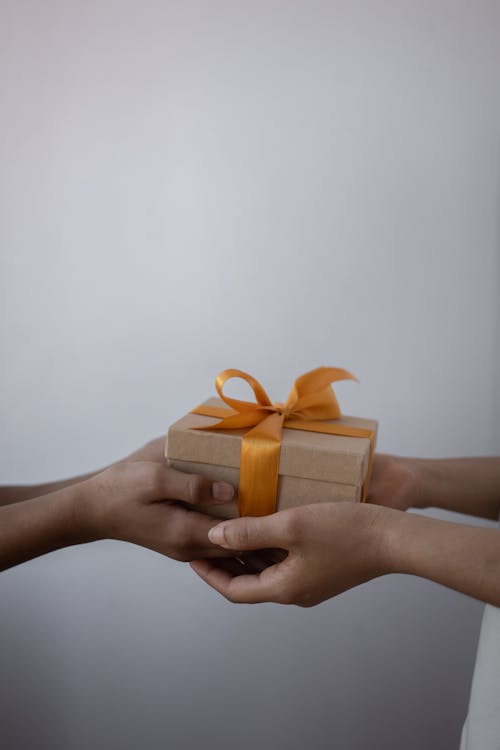Free Hands exchanging a wrapped gift box with an orange ribbon, symbolizing generosity. Stock Photo Free Hands exchanging a wrapped gift box with an orange ribbon, symbolizing generosity. Stock Photo