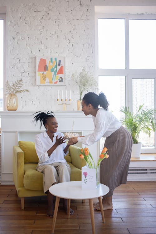 A Woman in Brown Skirt Giving Cake to the Woman Sitting on the Chair