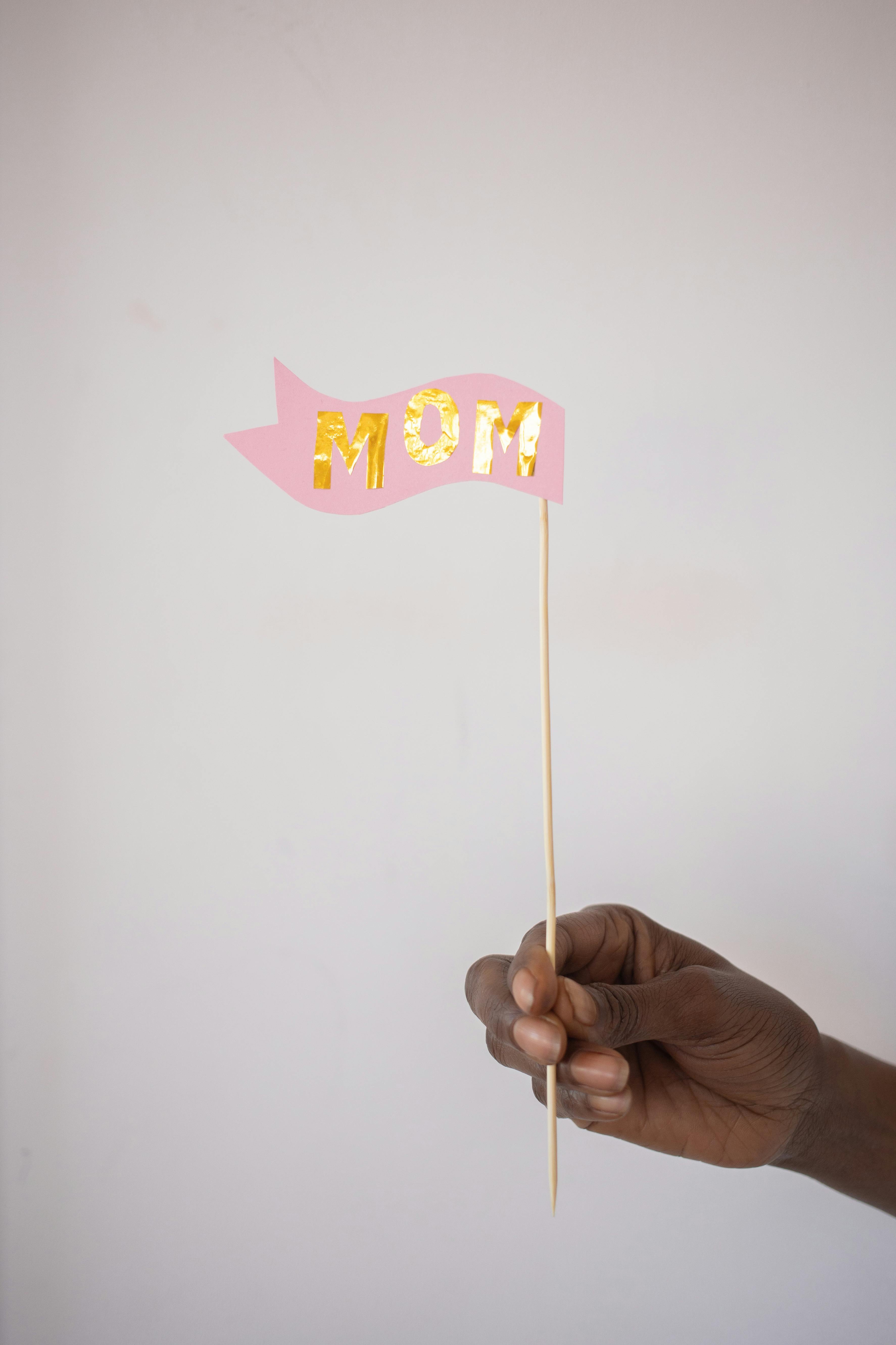 Close-up of a hand holding a pink 'Mom' sign, perfect for Mother's Day.