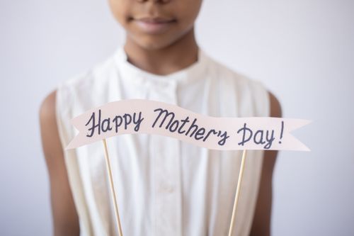 Free Child holding a decorative 'Happy Mother's Day!' sign, perfect for celebrating motherhood. Stock Photo