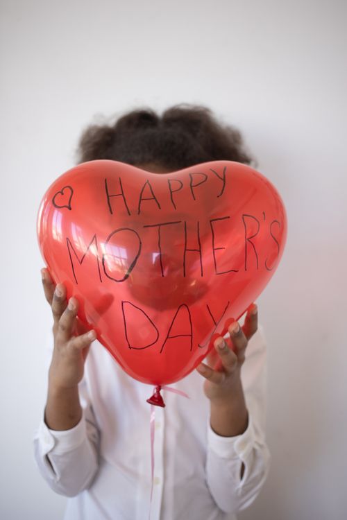 Free Child holding heart-shaped balloon with 'Happy Mother's Day' message. Celebrate with love. Stock Photo