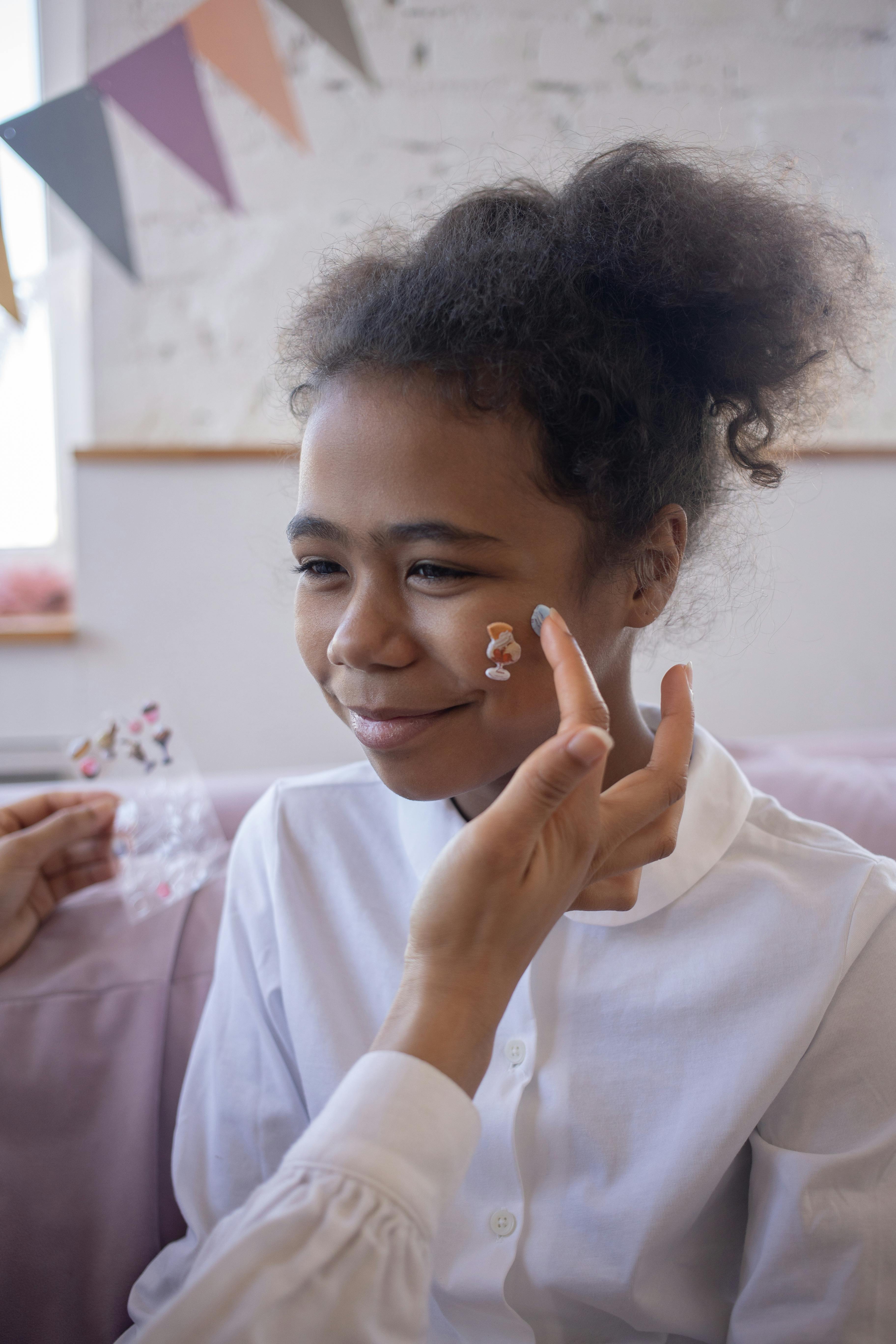 Smiling girl with face stickers applied, indoors in a playful setting.