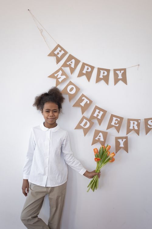 Free A cheerful young girl holds tulips under a Mother's Day banner indoors. Stock Photo