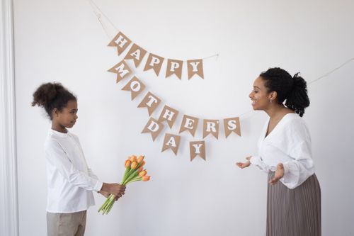 Free A smiling mother and daughter celebrate Mother's Day with tulips and a decorative banner indoors. Stock Photo