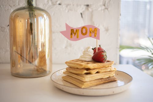 Stack of waffles with strawberries, whipped cream, and a 'MOM' flag, perfect for Mother's Day.