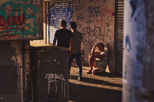 Free Two individuals stand while another sits in an urban alley filled with graffiti art. Stock Photo