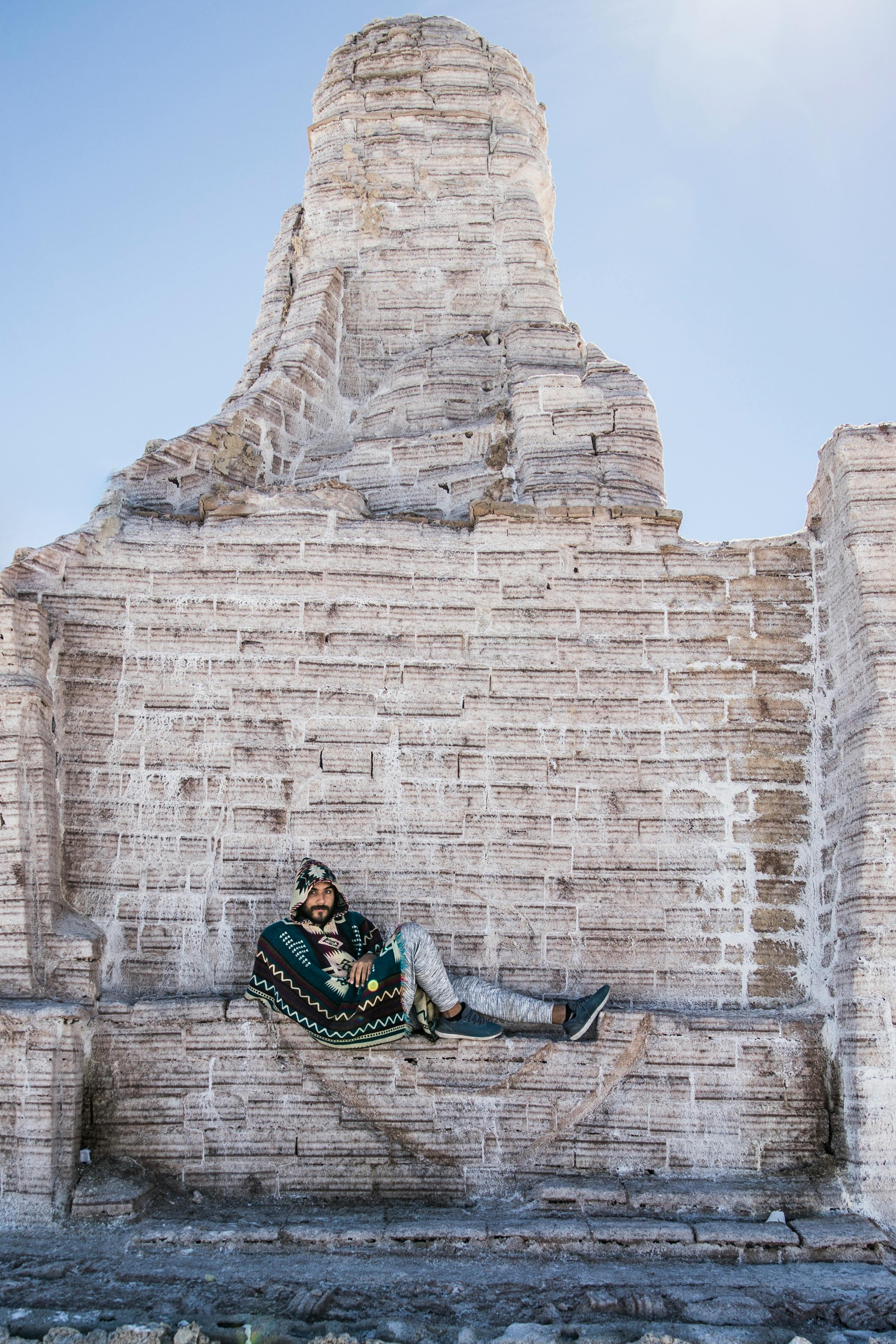 Hispanic man lounging against unique salt monument in Salar de Uyuni, Bolivia.