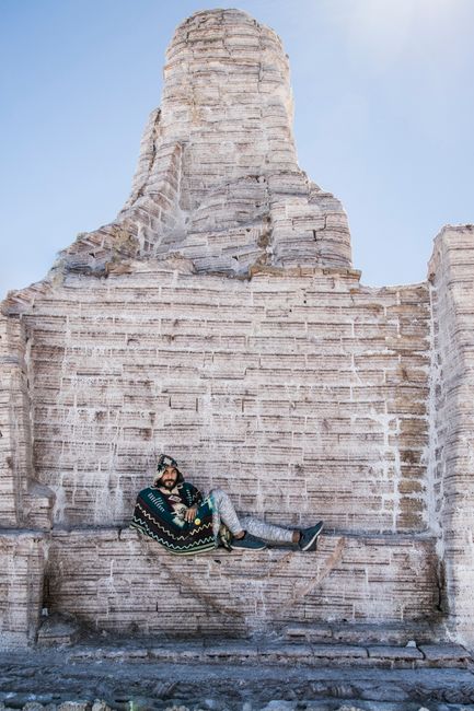 Hispanic man lounging against unique salt monument in Salar de Uyuni, Bolivia.