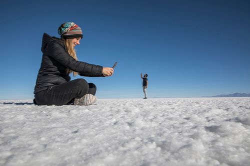 Free A woman takes a creative perspective photo of a man at the expansive Uyuni Salt Flats in Bolivia. Stock Photo