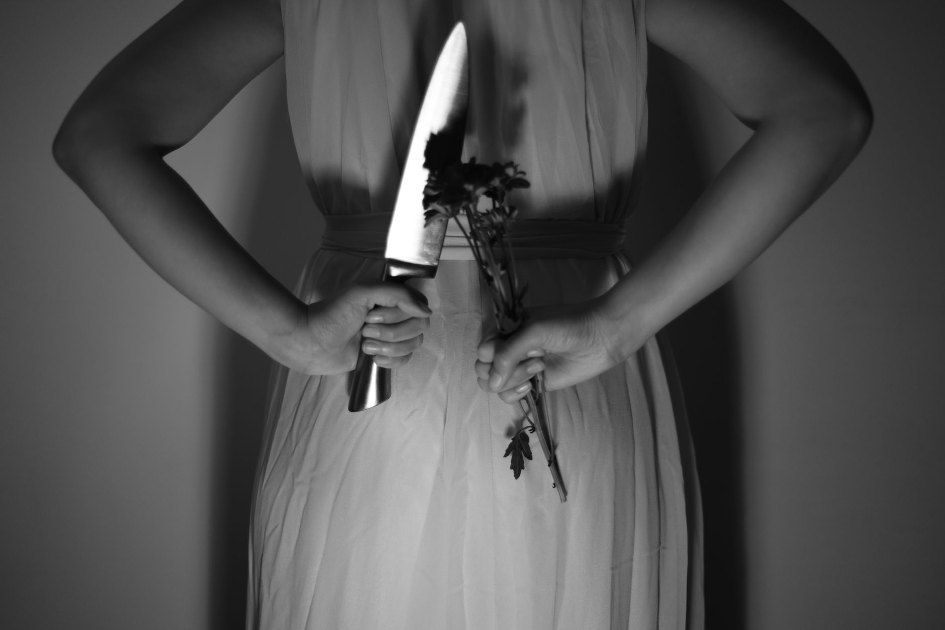 A woman holds a knife and a flower, creating a mysterious and dramatic scene in black and white.