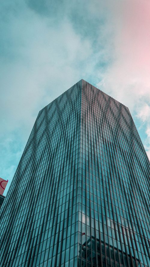 Free A modern skyscraper with a reflective glass facade reaching into a cloudy sky from a low angle view. Stock Photo