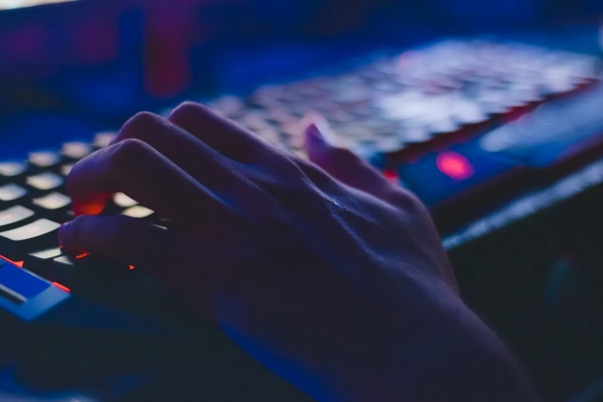 A hand resting on a backlit keyboard in a dark room, lit in blue and red.