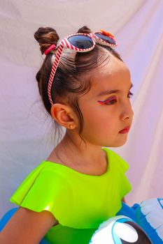 Adorable child posing with sunglasses and neon swimsuit, embodying summer fun.