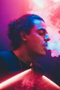 Young man exhaling smoke in neon lights