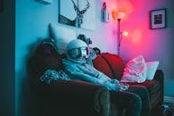 Anonymous guy in VR helmet sitting on sofa with controller while playing video game in cozy room with dark light