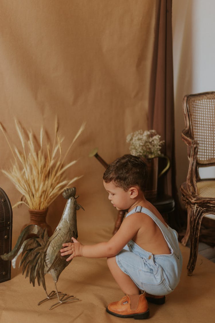 A Cute Boy Touching A Rooster Sculpture 