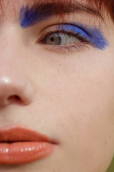 Detailed close-up portrait highlighting blue eyeshadow and orange lipstick against fair skin.