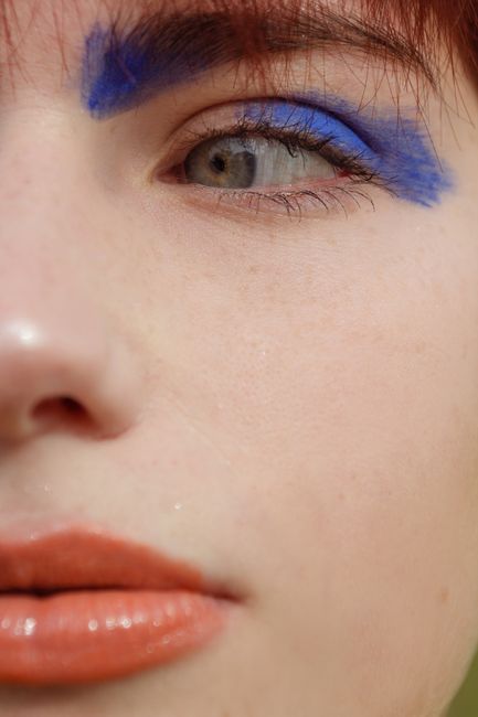 Detailed close-up portrait highlighting blue eyeshadow and orange lipstick against fair skin.