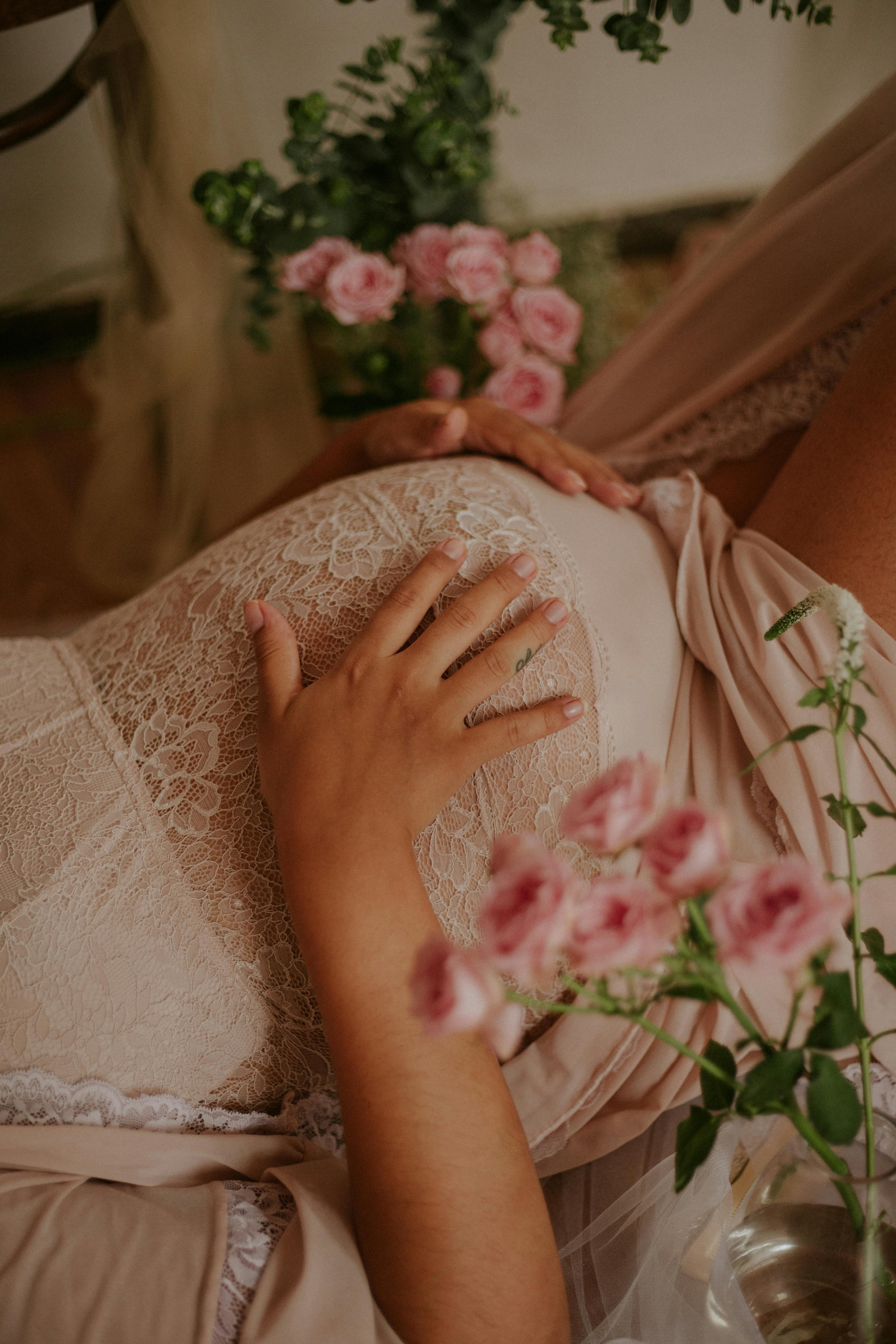 pregnant woman in beige lace dress holding her belly