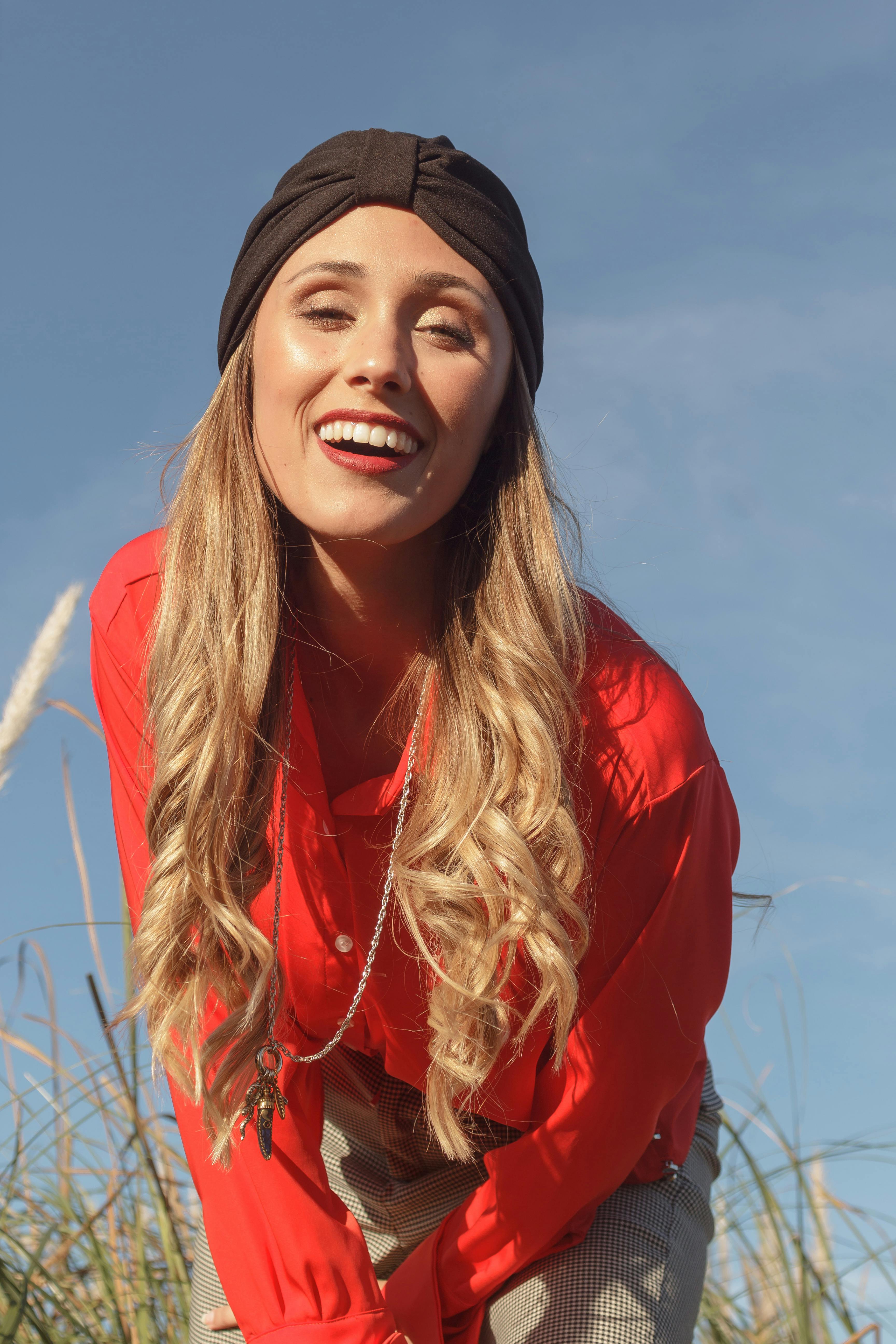 Smiling woman in a red outfit posing outdoors under a clear blue sky.