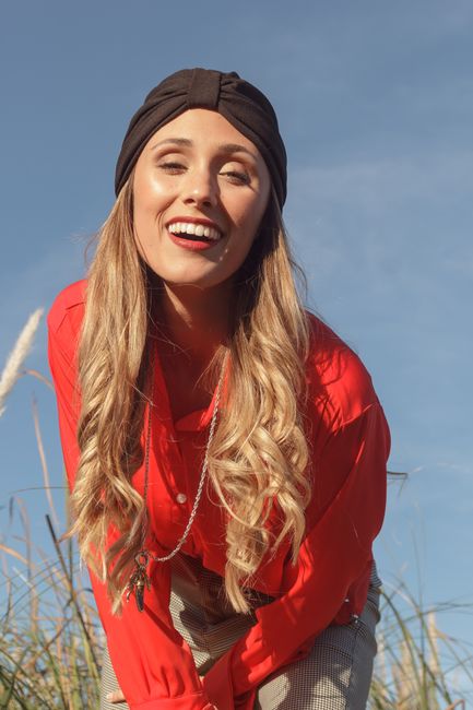 Smiling woman in a red outfit posing outdoors under a clear blue sky.