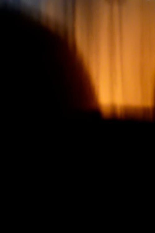 Dark shadow in yellow light of lamp at home with curtains in evening