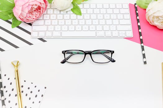 A modern feminine workspace with eyeglasses, keyboard, and flowers, creating an elegant and contemporary office vibe.