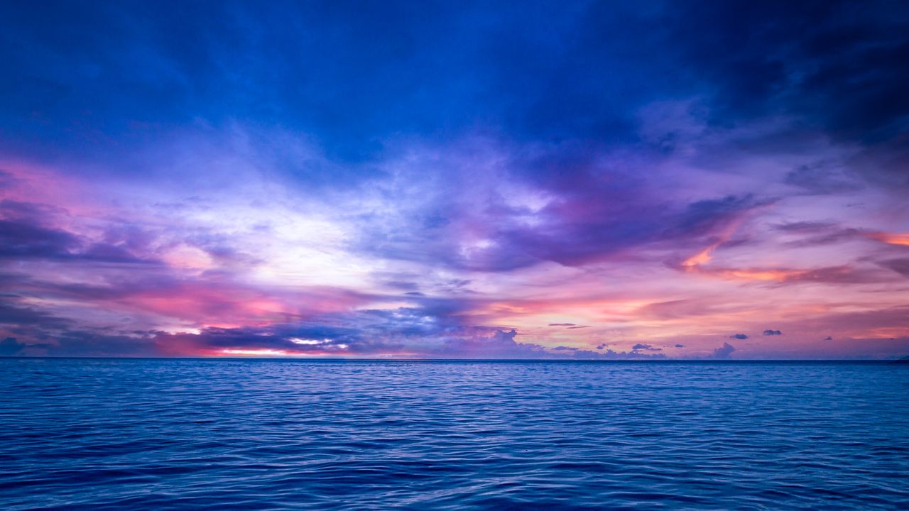 stunning view of an ocean at sunset with vibrant purple and blue skies