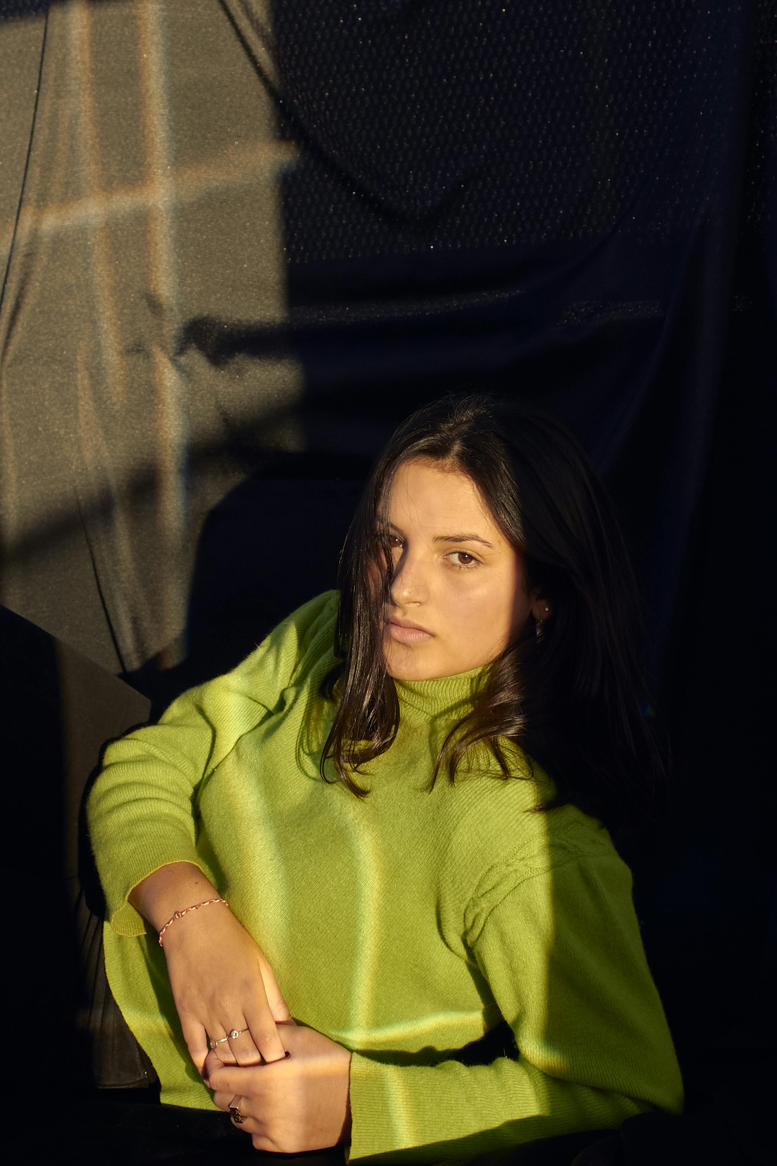 Woman wearing a bright green sweater, captured in dramatic light and shadows, conveying a serious mood.