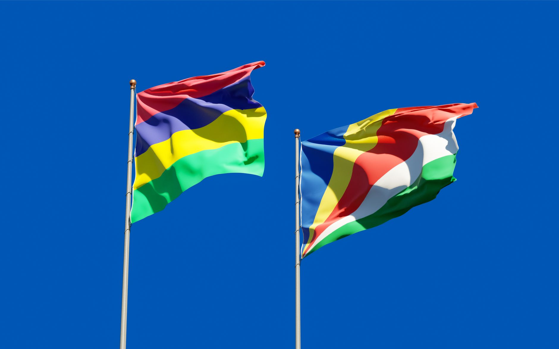 Flags of Mauritius and Seychelles waving on flagpoles with a clear blue sky backdrop, representing unity. — free online jigsaw puzzle on JigsawPuzzlesFreeOnline.org