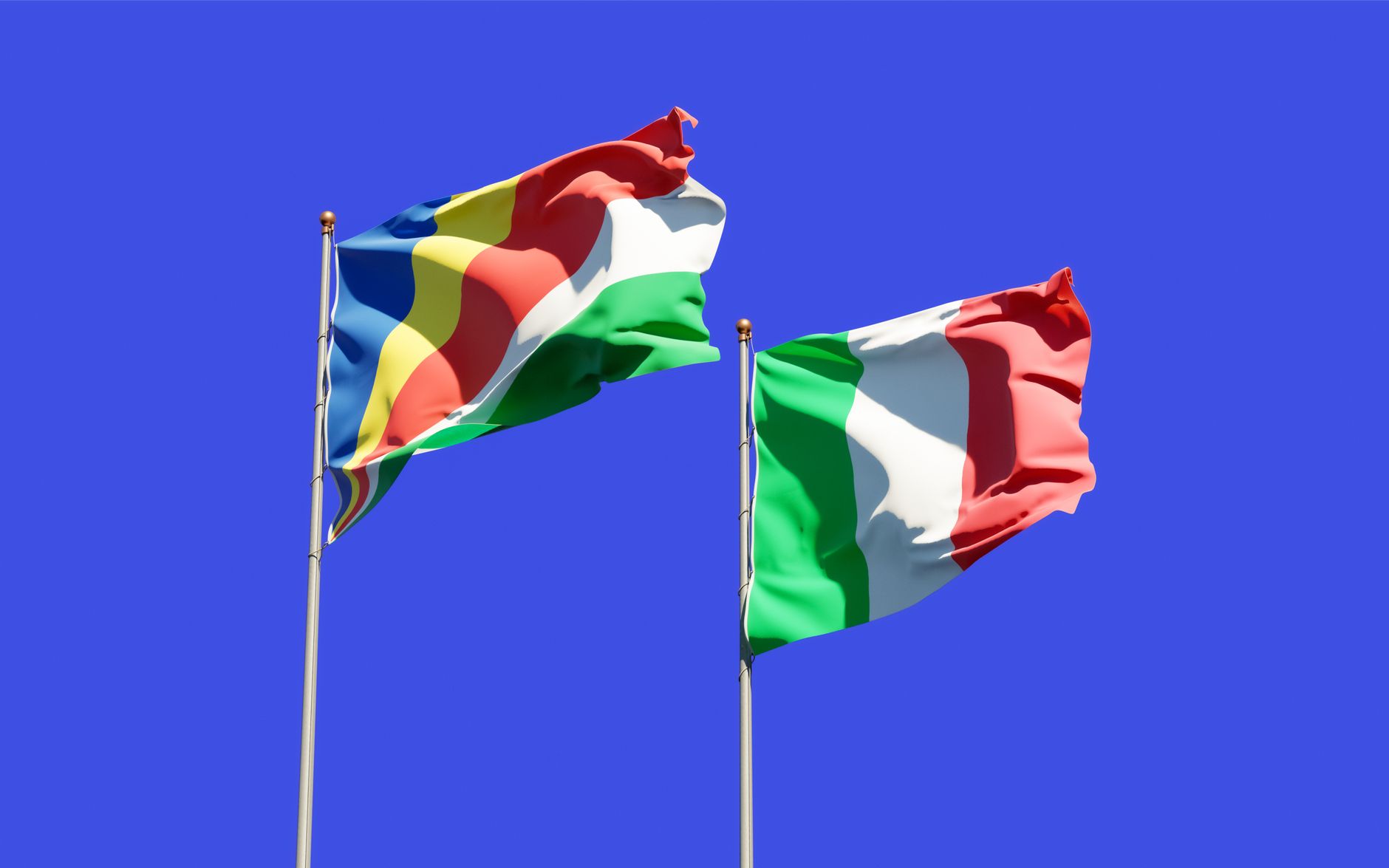 Colorful Seychelles and Italian flags waving on flagpoles under a clear blue sky.
