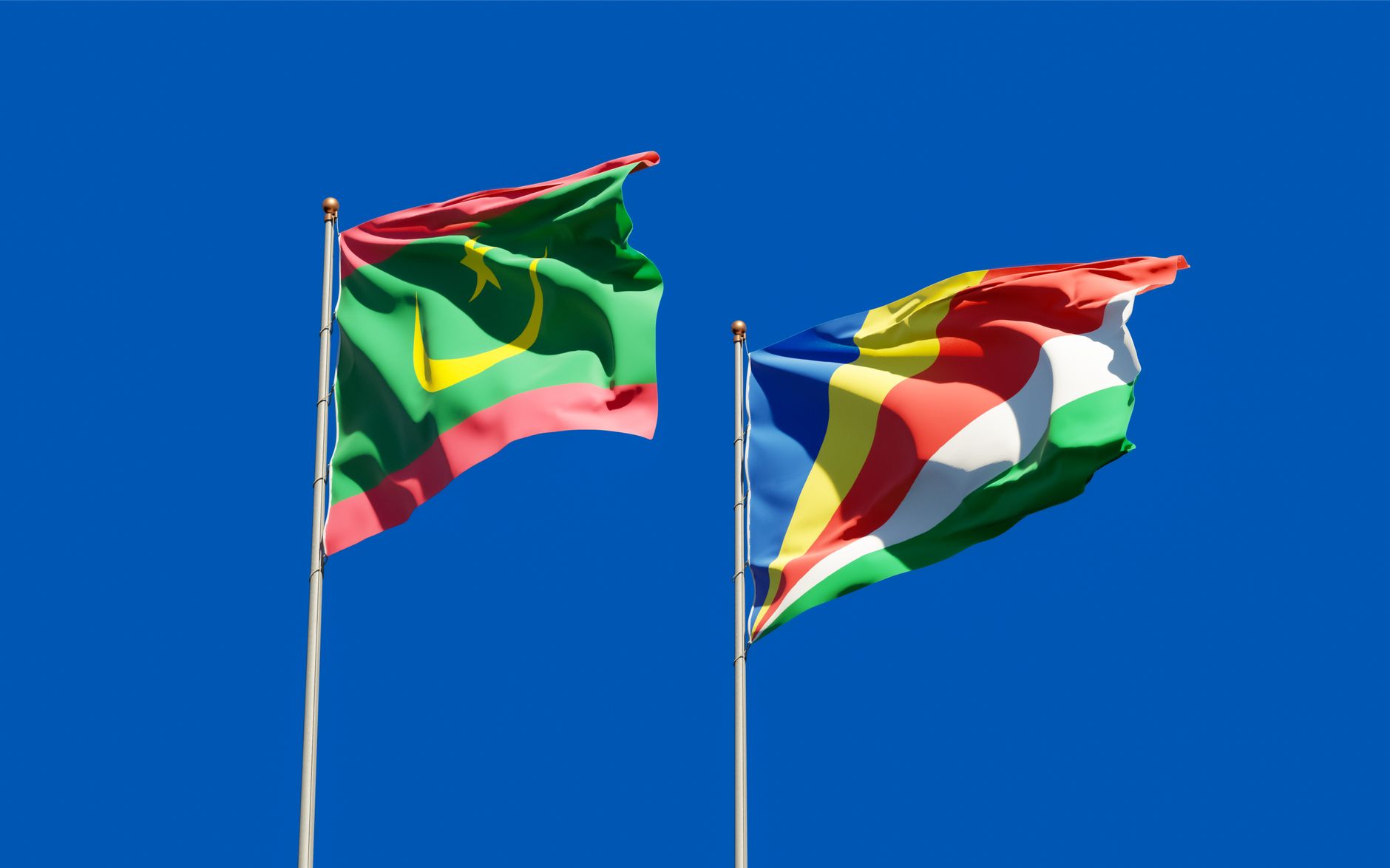 National flags of Mauritania and Seychelles waving against a clear blue sky, symbolizing unity. — free online jigsaw puzzle on JigsawPuzzlesFreeOnline.org