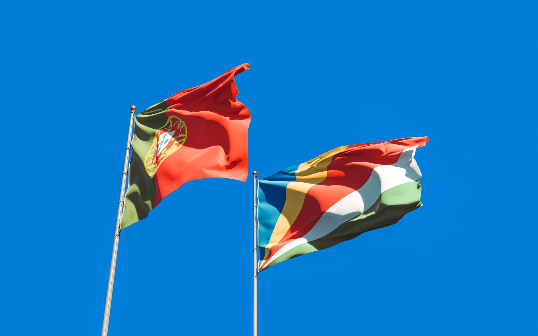 Portuguese and Seychelles flags waving against a clear blue sky, symbolizing unity and patriotism.