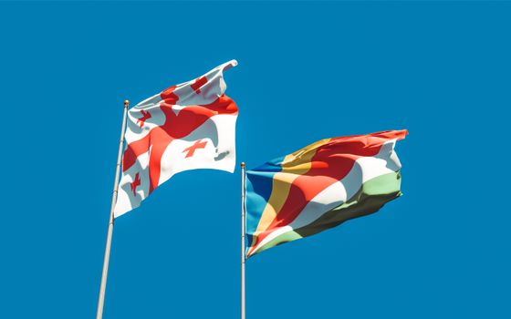Vibrant image of Georgia and Seychelles flags waving with blue sky backdrop, symbolizing unity and cultural pride., free online jigsaw puzzle on JigsawPuzzlesFreeOnline.org