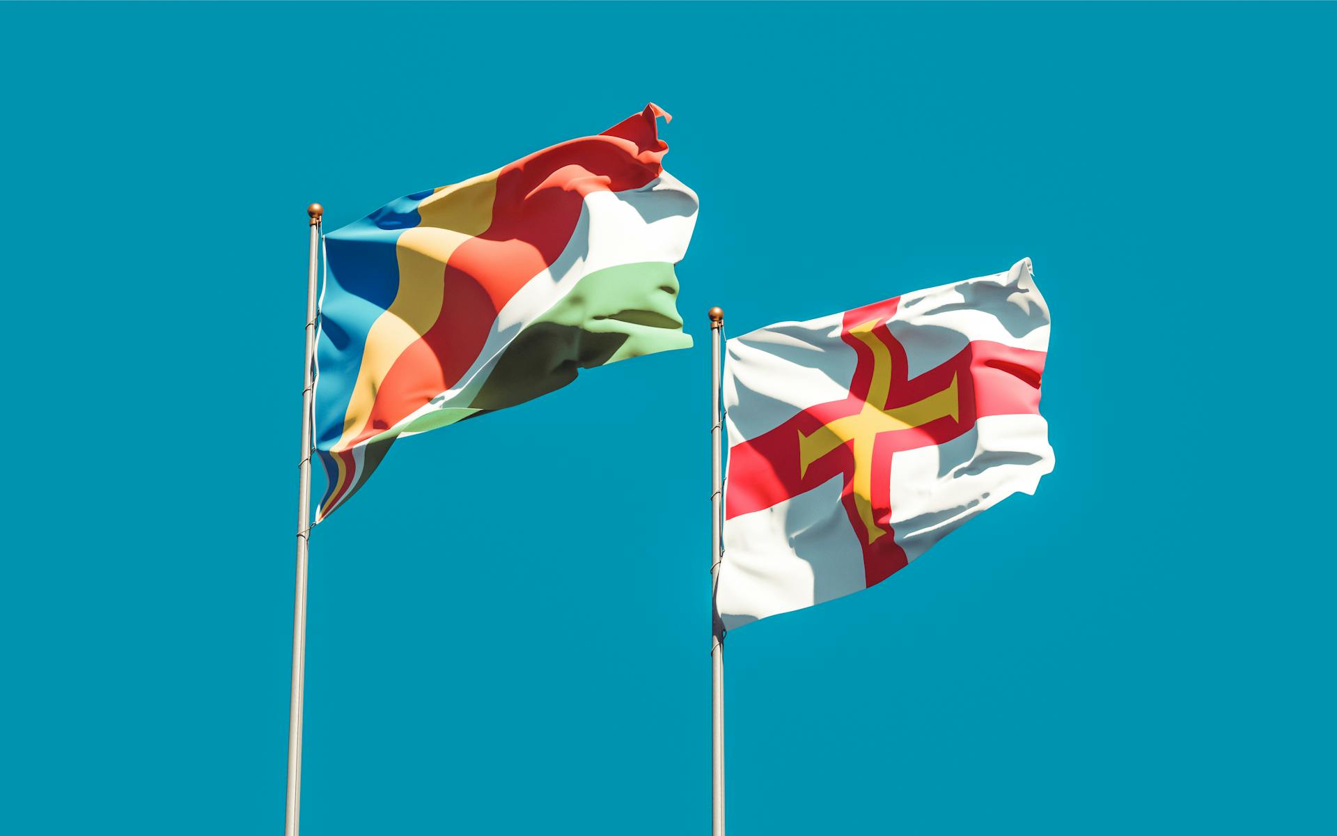 Seychelles and Guernsey flags waving against a bright blue sky, symbolizing unity and pride.