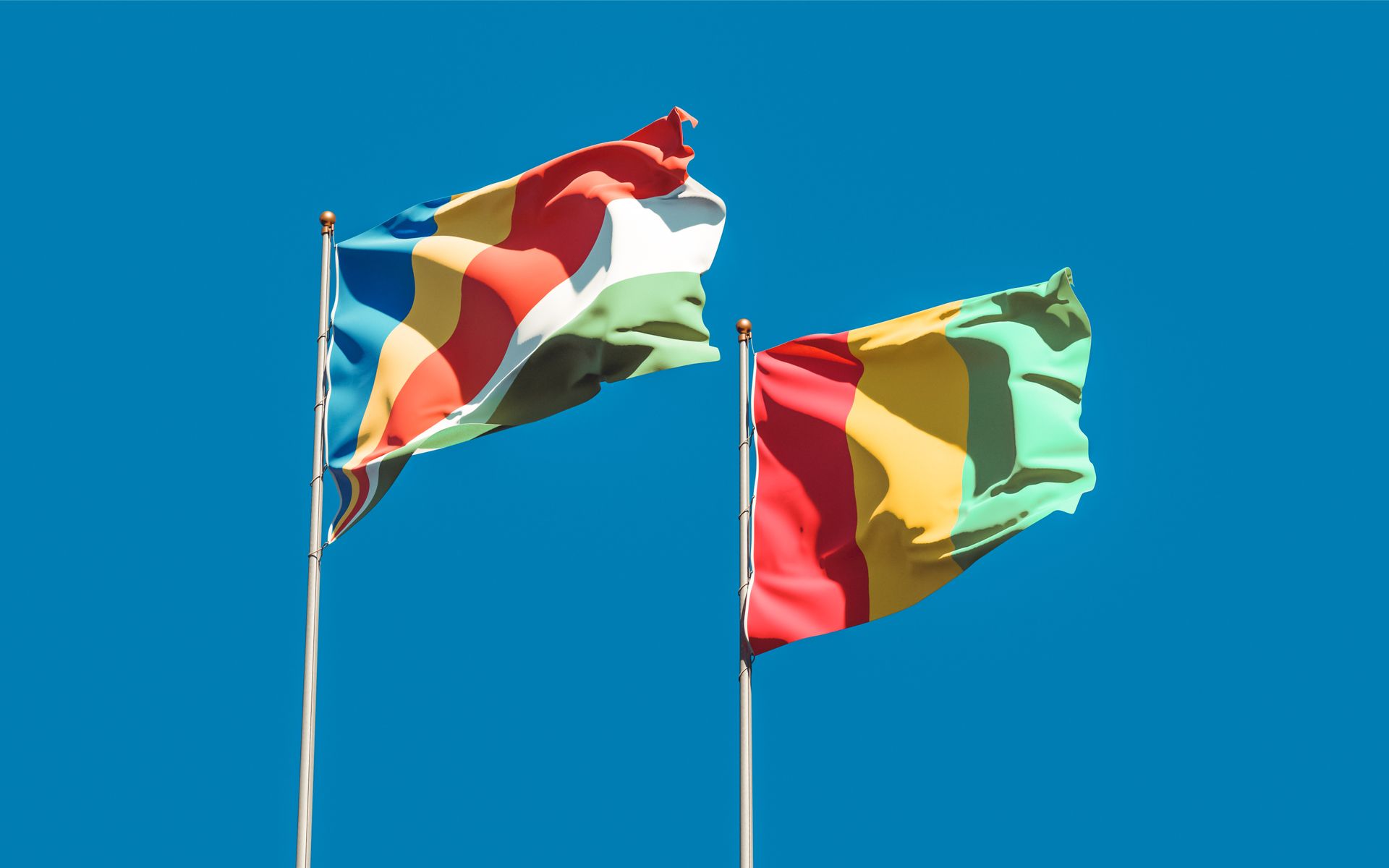 Vibrant national flags of Seychelles and Guinea waving against a clear blue sky, symbolizing unity and patriotism.