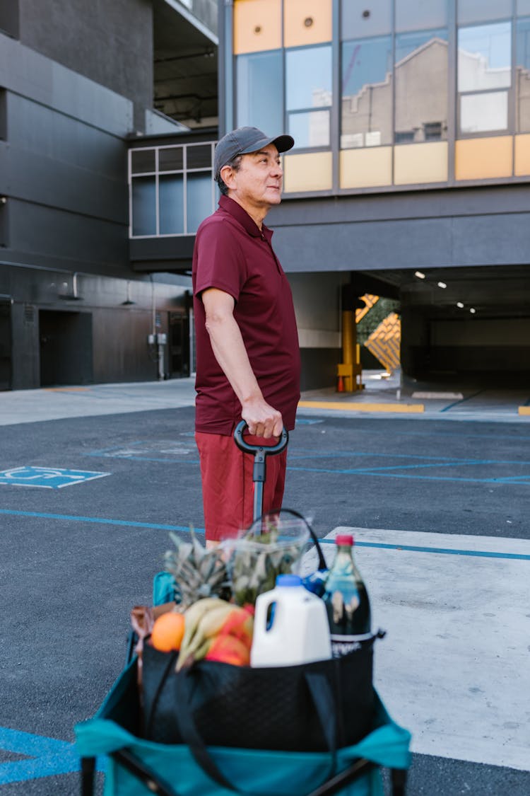 A Man In A Maroon Shirt Holding A Cart Of Groceries