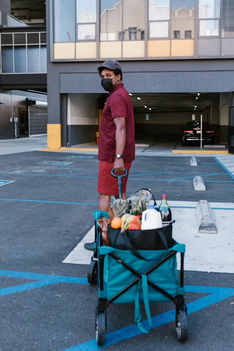 A Man In A Maroon Shirt Holding A Cart Of Groceries