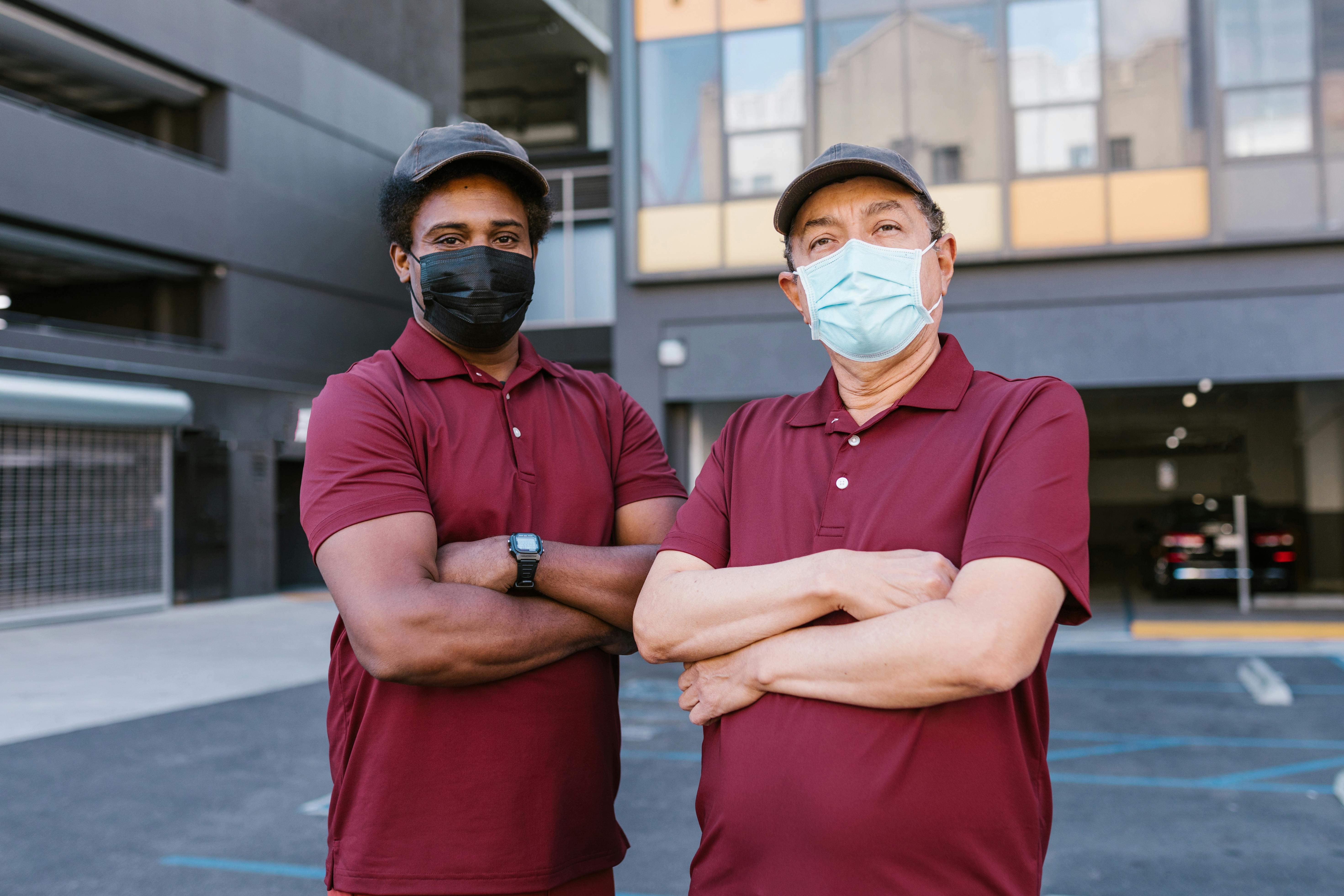 Two men wearing matching maroon uniforms and face masks standing confidently outdoors.