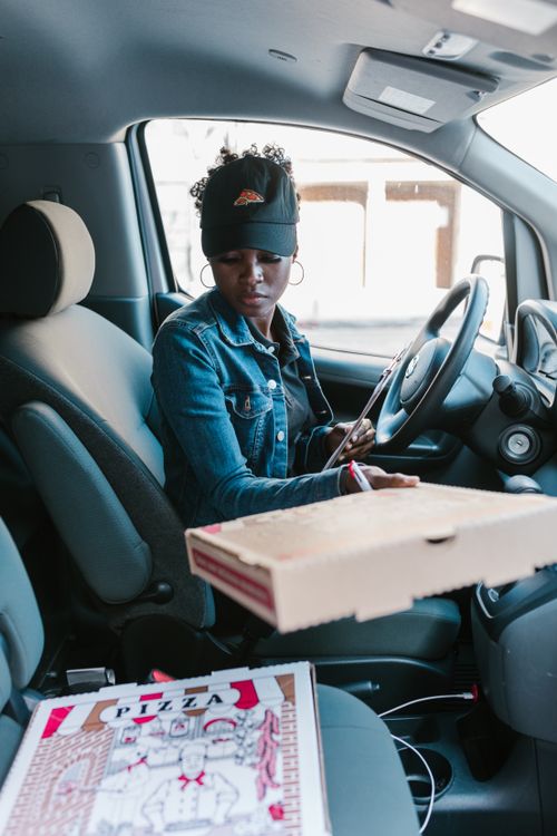 Free Woman in a car preparing to deliver pizza with a clipboard. Perfect for delivery and career themes. Stock Photo