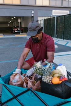 A delivery man in a maroon shirt organizes groceries in a parking lot.