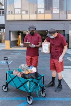 Grocery and package delivery workers in masks, outdoors, with cart in a parking lot.