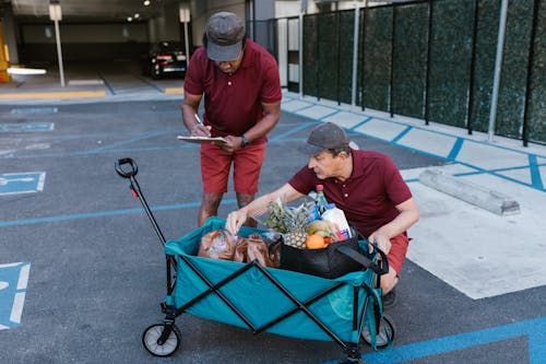 Man in Red Crew Neck T-shirt and Blue Denim Jeans Pushing a Cart With Fruits