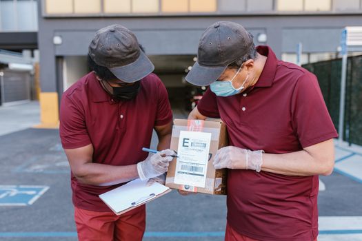 Two delivery service workers wearing masks and gloves checking a package outdoors.