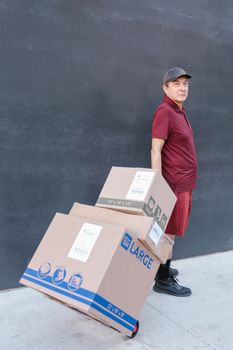 Delivery man in uniform pulling a trolley with large cardboard boxes outside on a clear day.