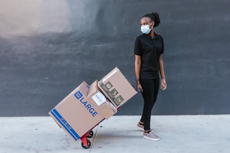 Woman In Black Polo Shirt Pulling The Trolley Push Cart With Shipping Boxes