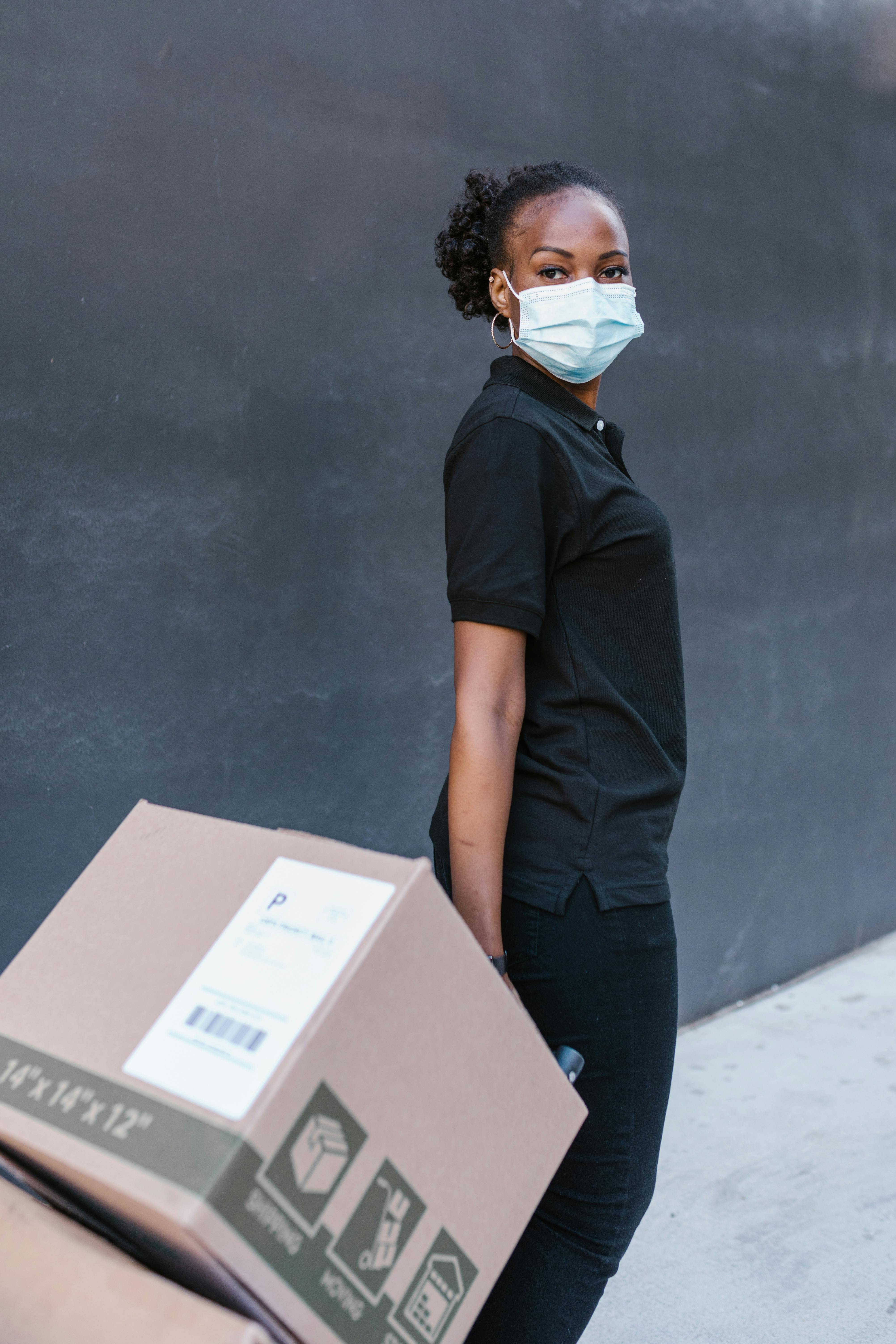woman in black long sleeve shirt and blue denim jeans holding brown cardboard box