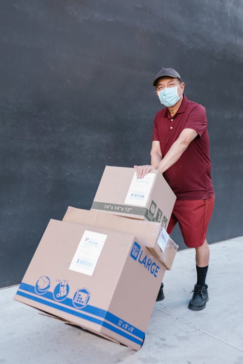 Free Man in Red Polo Shirt and Red Shorts Holding Brown Cardboard Box Stock Photo