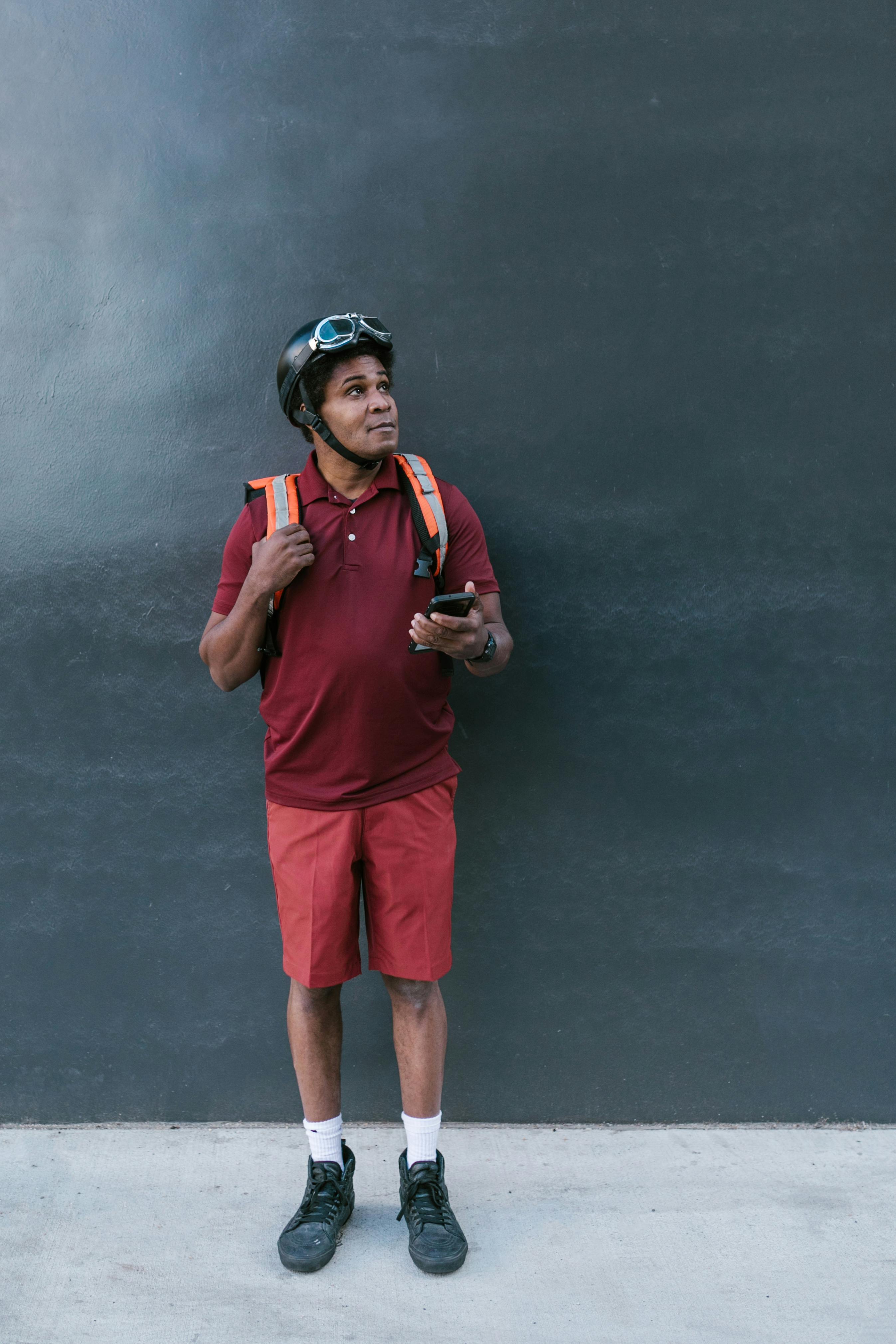 man with food delivery bag holding his smartphone while looking up