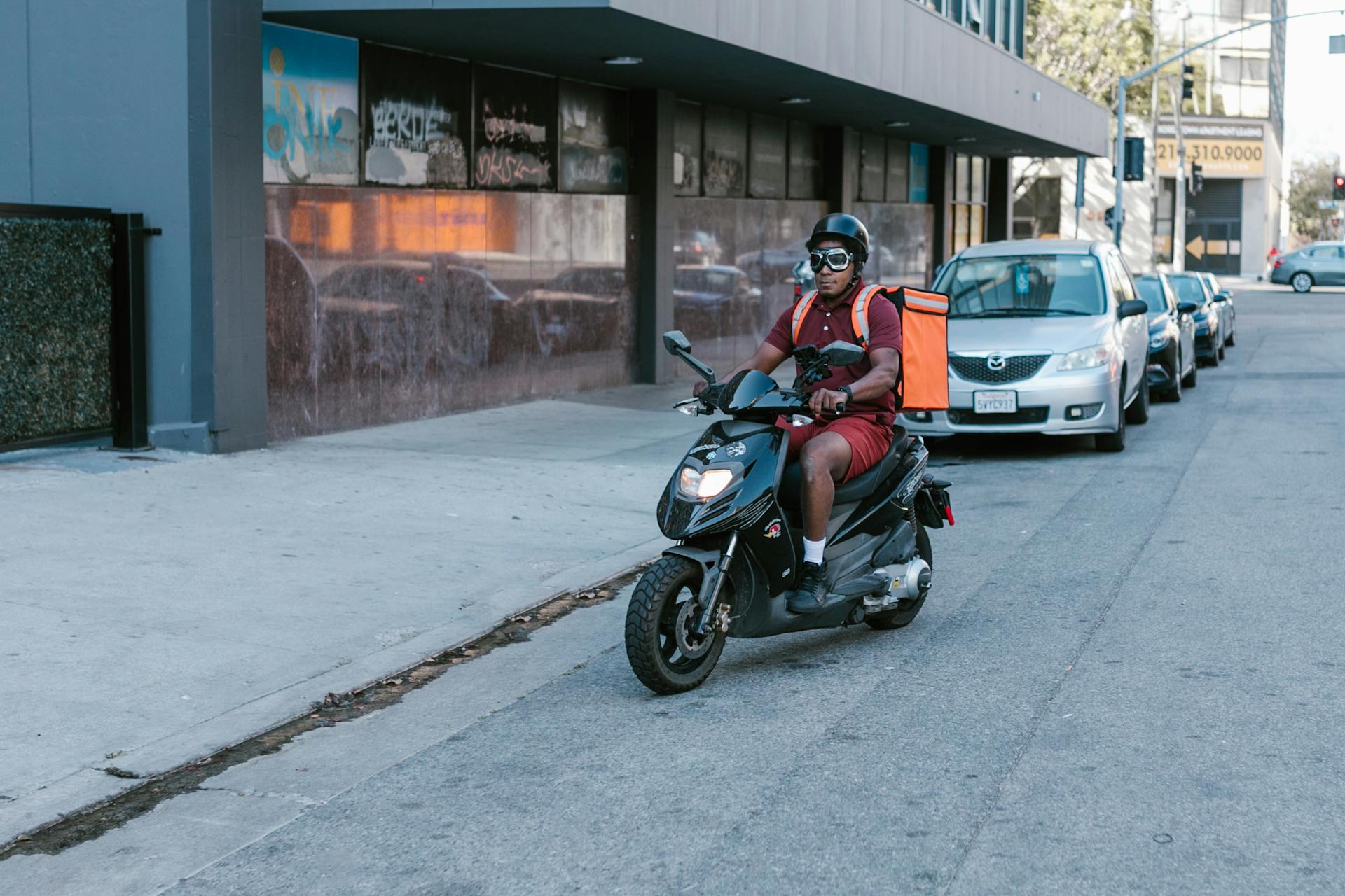 African American man delivering on a scooter in the city wearing safety gear.